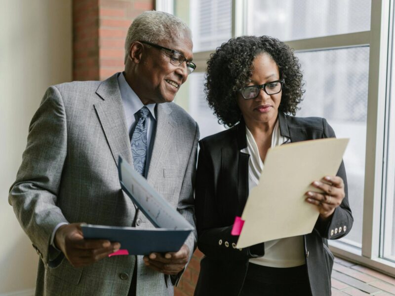An elderly man and a woman looking at a manilla folder while having a conversation.