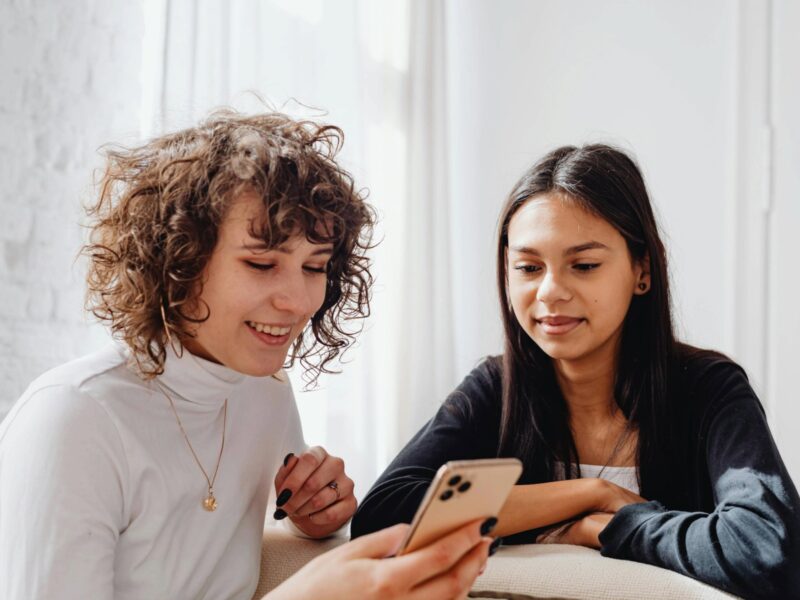 Women smiling using cellphone together.