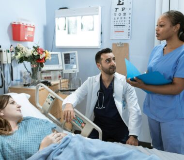 In a hospital room, a doctor and nurse discuss a treatment plan in front of the patient.