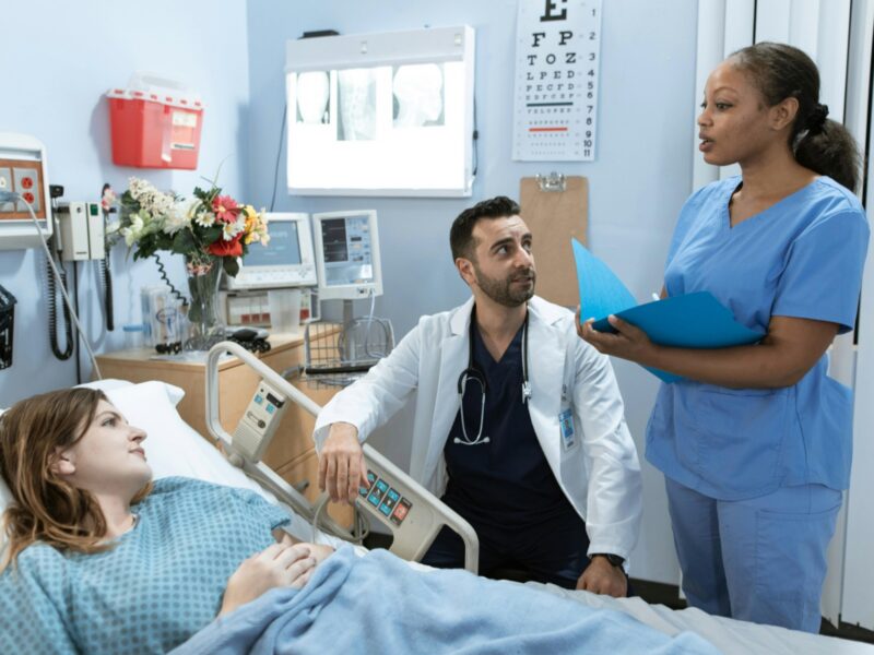 In a hospital room, a doctor and nurse discuss a treatment plan in front of the patient.