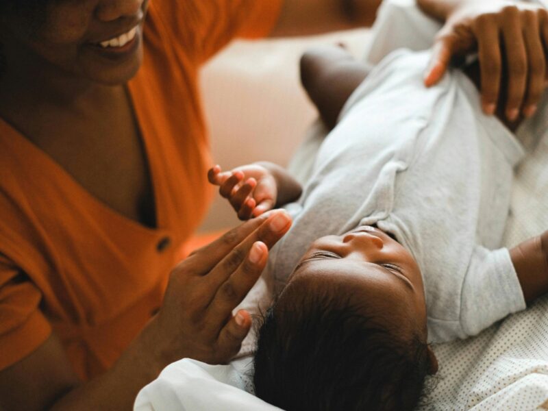 a black mother engages with her newborn baby on a couch indoors
