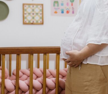A pregnant woman stands beside a crib.
